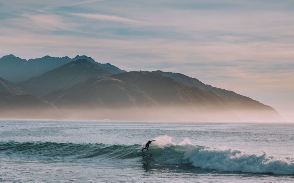 A surfer on a peeling left at Raglan, New Zealand, with hills behind.