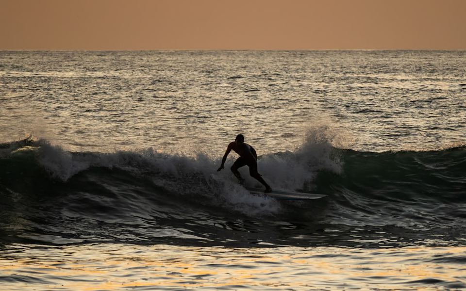 A surfer silhouetted on a wave at sunset, Santa Teresa, Costa Rica.