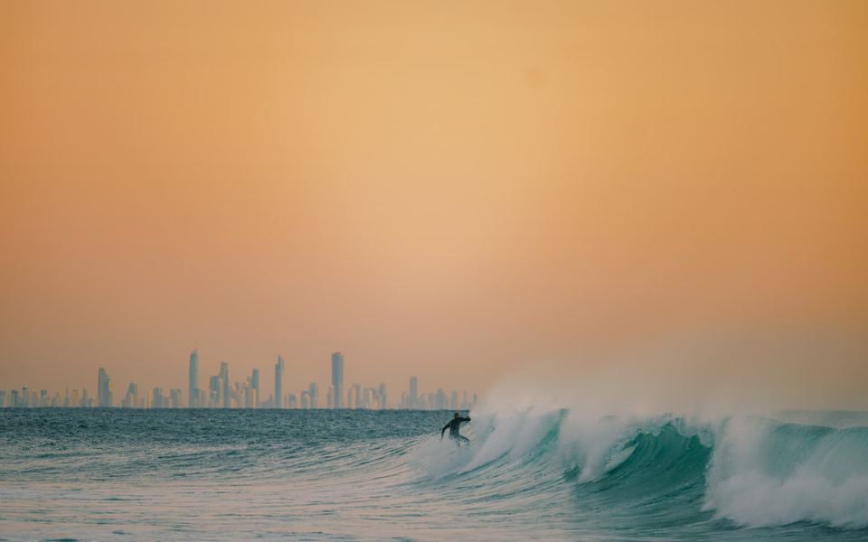 A surfer on a wave at Snapper Rocks, with the Gold Coast skyline behind.